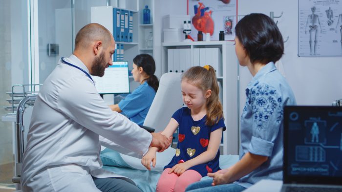 Doctor checking child injured arm and talking with mother. Healthcare practitioner physician specialist in medicine providing health care service radiographic treatment examination in hospital cabinet
